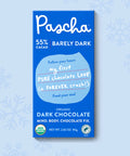 The front of Pascha Chocolate's 55% Barely Dark Chocolate Bar with half of the exposed bar sticking out of the top of the packaging