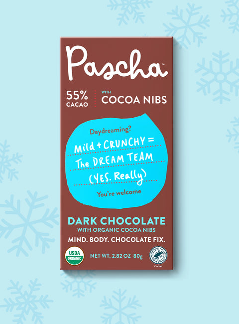 The front of Pascha Chocolate's 55% with Cocoa Nibs Dark Chocolate Bar with half of the exposed bar sticking out of the top of the packaging