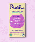 The front of Pascha Chocolate's Vegan White Bar packaging on a light pink background with subtle snowflakes.