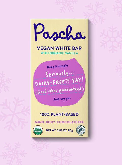 The front of Pascha Chocolate's Vegan White Bar packaging on a light pink background with subtle snowflakes.