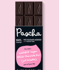 The front of Pascha Chocolate's 100% No Sugar Added with Cocoa Nibs Dark Chocolate Bar with half of the exposed bar sticking out of the top of the packaging