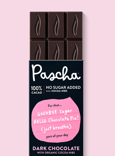 The front of Pascha Chocolate's 100% No Sugar Added with Cocoa Nibs Dark Chocolate Bar with half of the exposed bar sticking out of the top of the packaging
