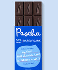 The front of Pascha Chocolate's 55% with Barely Dark Chocolate Bar with half of the exposed bar sticking out of the top of the packaging