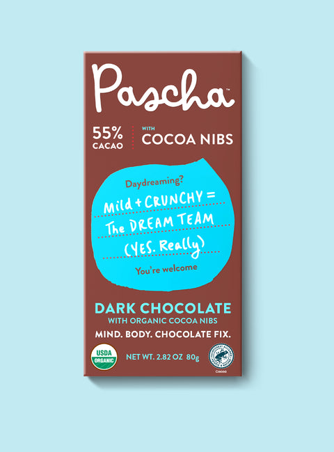 The front of Pascha Chocolate's 55% with Cocoa Nibs Dark Chocolate Bar with half of the exposed bar sticking out of the top of the packaging