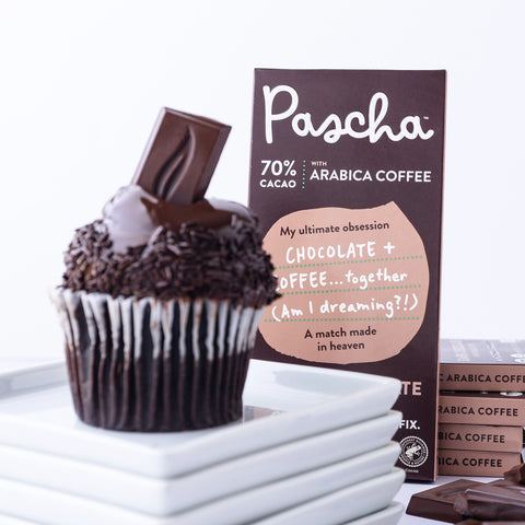 A dark chocolate cupcake is resting on a stack of white small plates and there is a 70% Dark Chocolate Arabica Coffee bar propped up behind the stack 