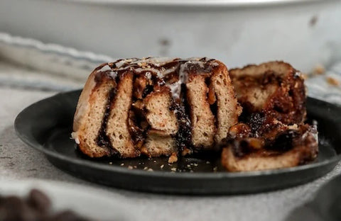 Cinnamon bun cut in half resting on a black plate resting on a grey speckled countertop