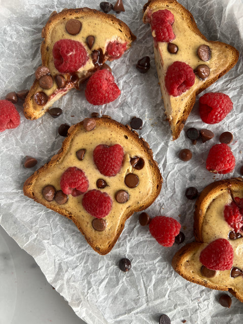Three pieces of french toast topped with raspberries and chocolate chips are resting on a counter on top of parchment paper. Two of the pieces are cut in half and the other is a full slice