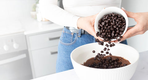 Woman pouring delicious Pascha chocolate baking chips into another white bowl in her kitchen.