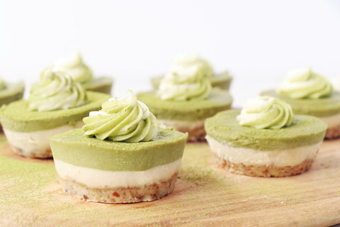 There are several matcha cheesecake rounds sitting on a wooden cutting board. 