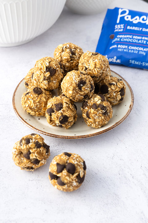 Several protein balls sit on a white plate with a brown trimmed edge, rested on a white and grey speckled countertop