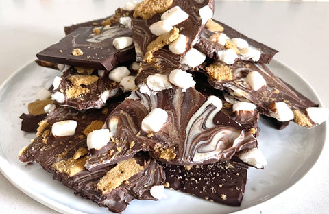 Chocolate graham cracker marshmallow bark cut up into large pieces and placed on a white plate stacked. 