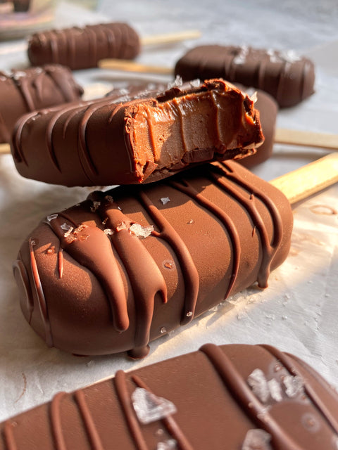 Chocolate Fudge Icecream Bars placed on parchment paper and there is one stacked on top of another with a bite taken out to show the delicious ice cream and fudge filled centre 