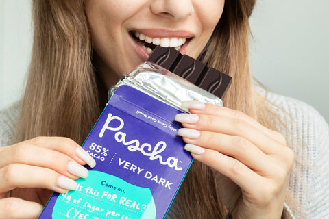 Close up shot of a woman taking a bite out of a partially unwrapped Pascha 85% Very Dark Chocolate Bar